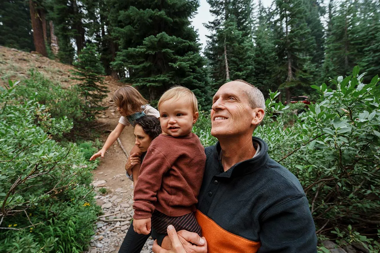 A family strolls through a wooded area, holding hands and enjoying nature with their young child.