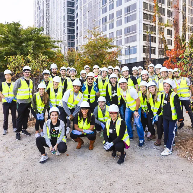 A group of individuals wearing safety vests and hard hats, engaged in a tree planting ceremony.