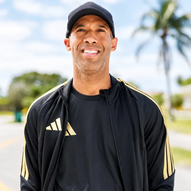 A man wearing a black and gold jacket and matching hat, standing confidently with a neutral expression.