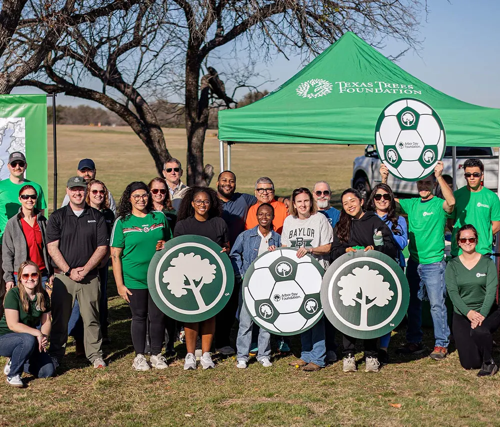 A group of people wearing green shirts and hats joyfully holds up a soccer ball, celebrating their team spirit.