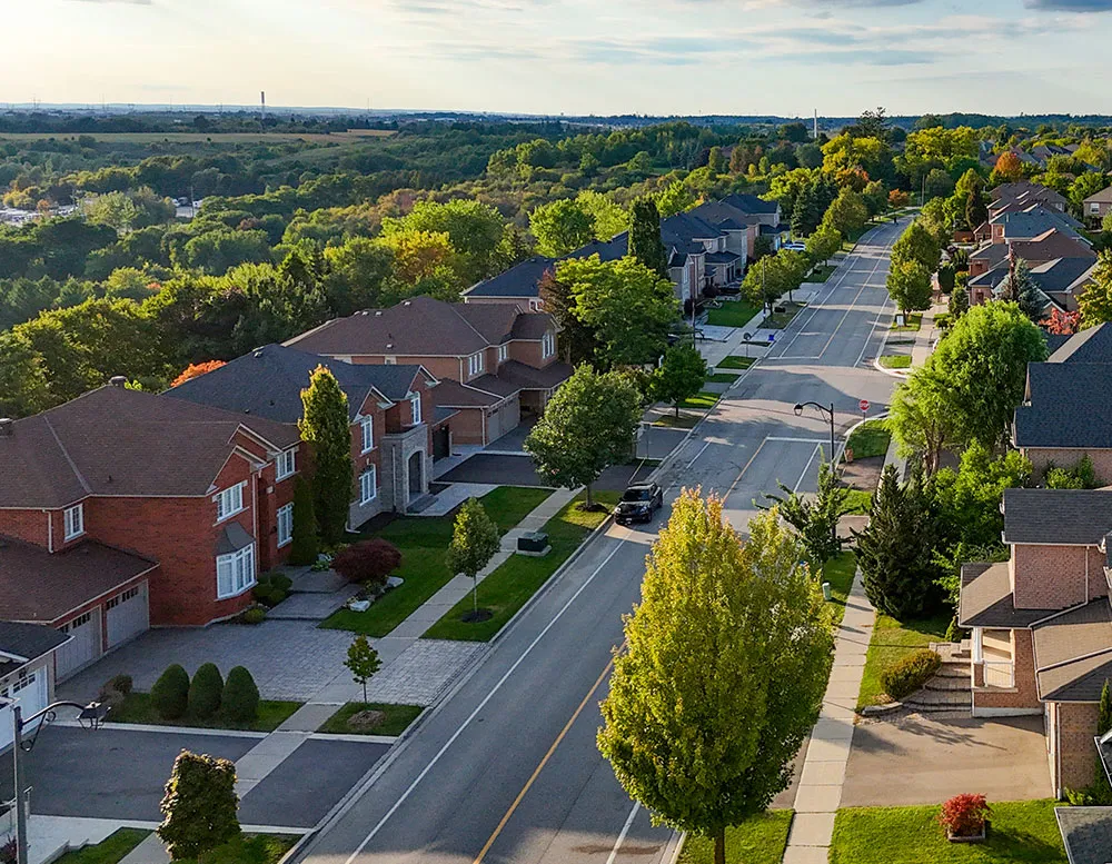A residential neighborhood featuring several houses surrounded by lush green trees under a clear blue sky.