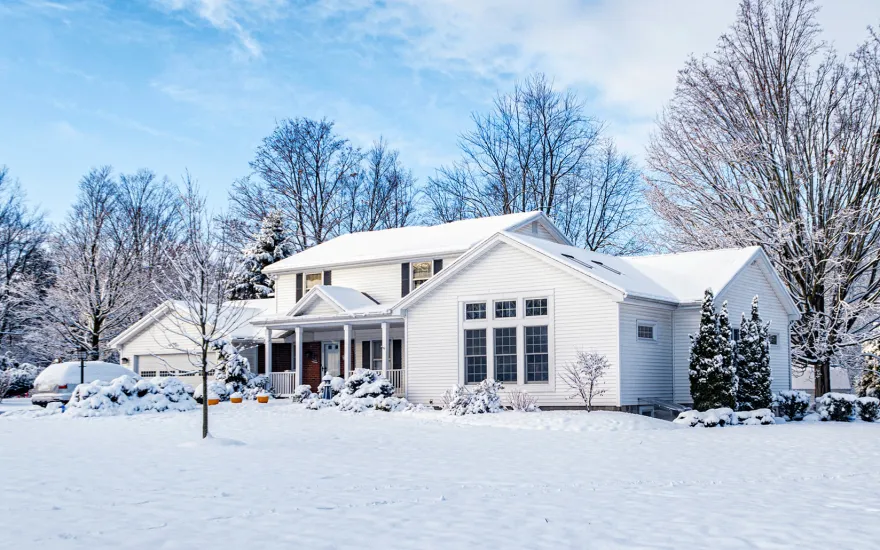 A white house surrounded by snow, illustrating strategic tree planting for warmth and reduced energy bills.