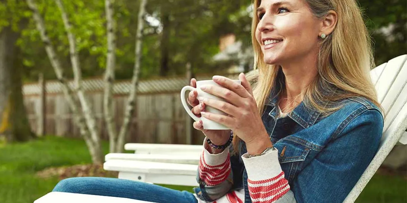 Woman sitting in a chair in her backyard enjoying a cup a coffee.