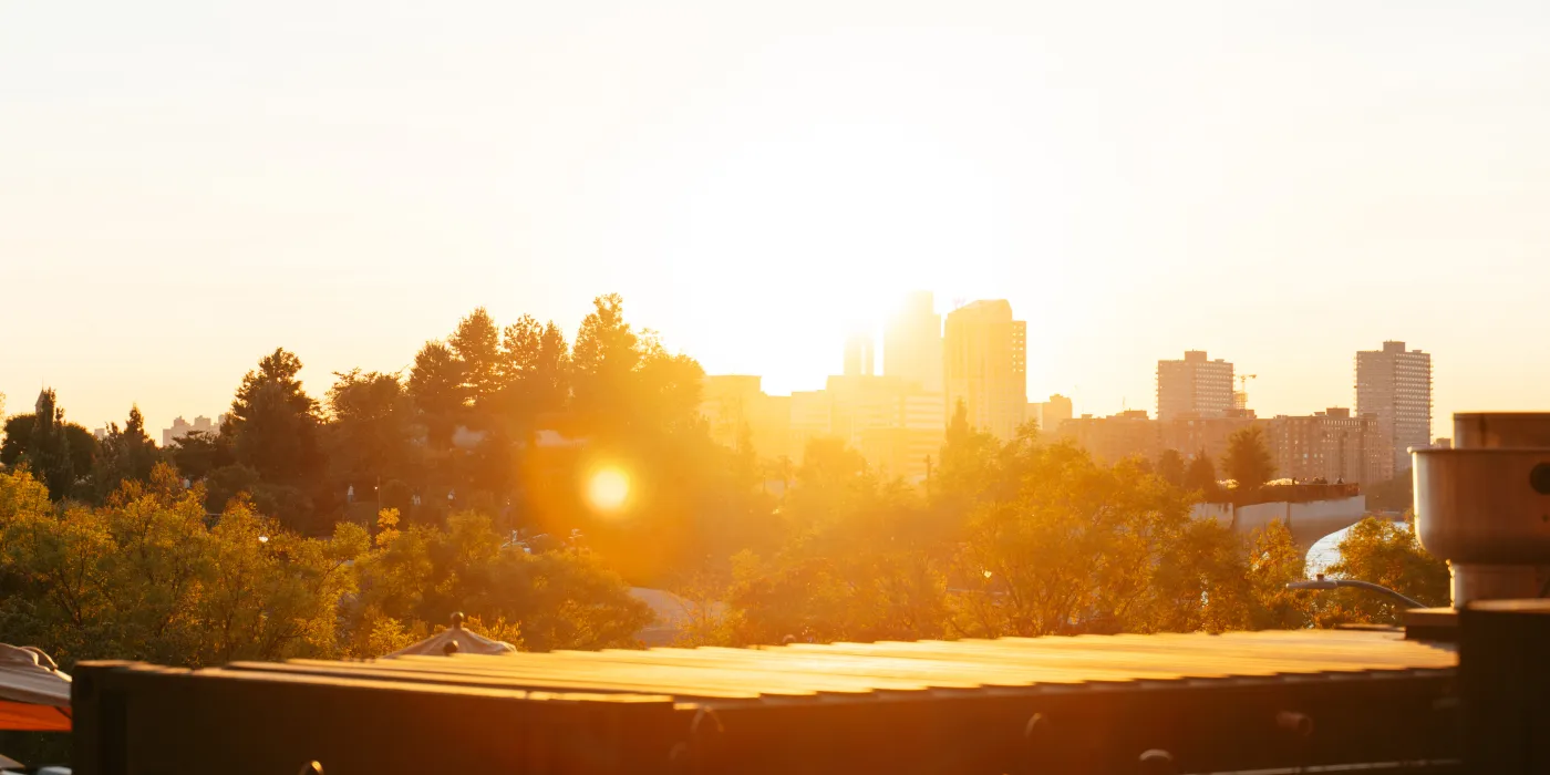 A vibrant sunset over a city skyline, casting warm light on trees and buildings, creating a serene evening atmosphere.
