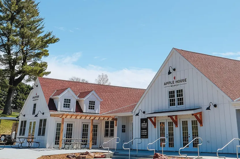 Exterior view of the Apple House Market, a charming white building with a red roof, surrounded by trees and a clear blue sky.