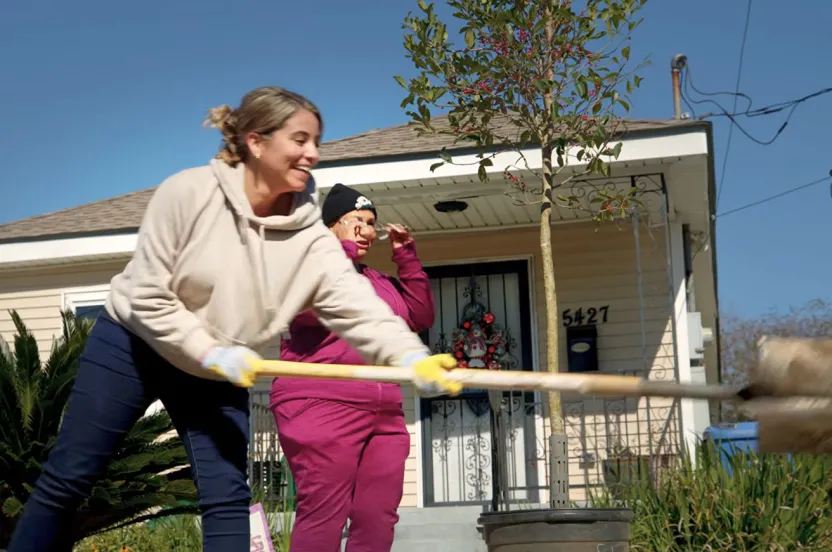 Two women are engaged in yard cleanup, using shovels to gather leaves and maintain the outdoor space.