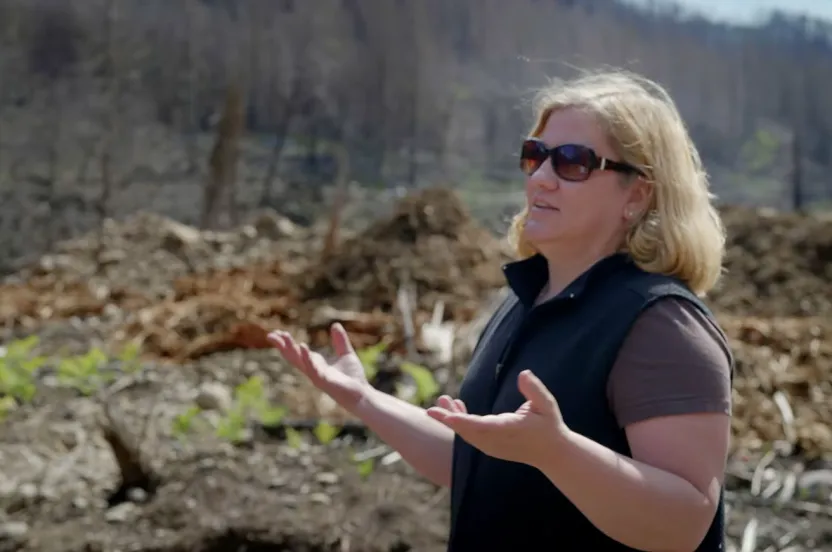 A woman wearing sunglasses stands confidently in front of a large pile of dirt, showcasing a construction or landscaping site.