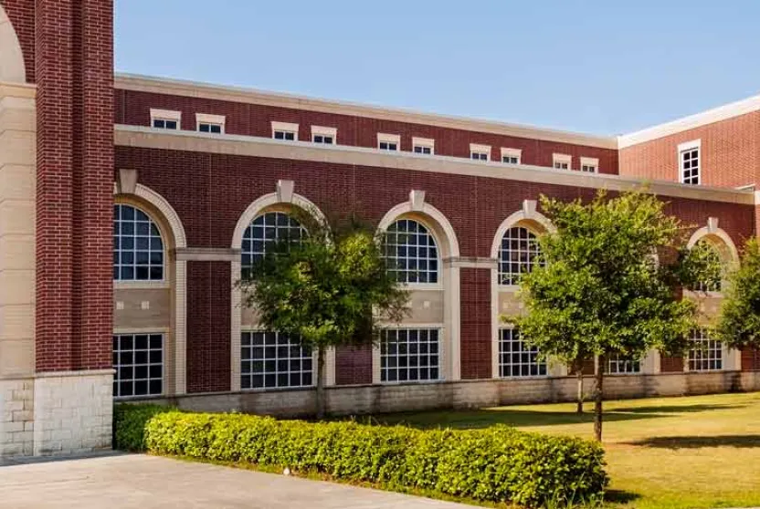 A large brick high school building with multiple windows surrounded by a lush grassy area, creating a welcoming outdoor space.
